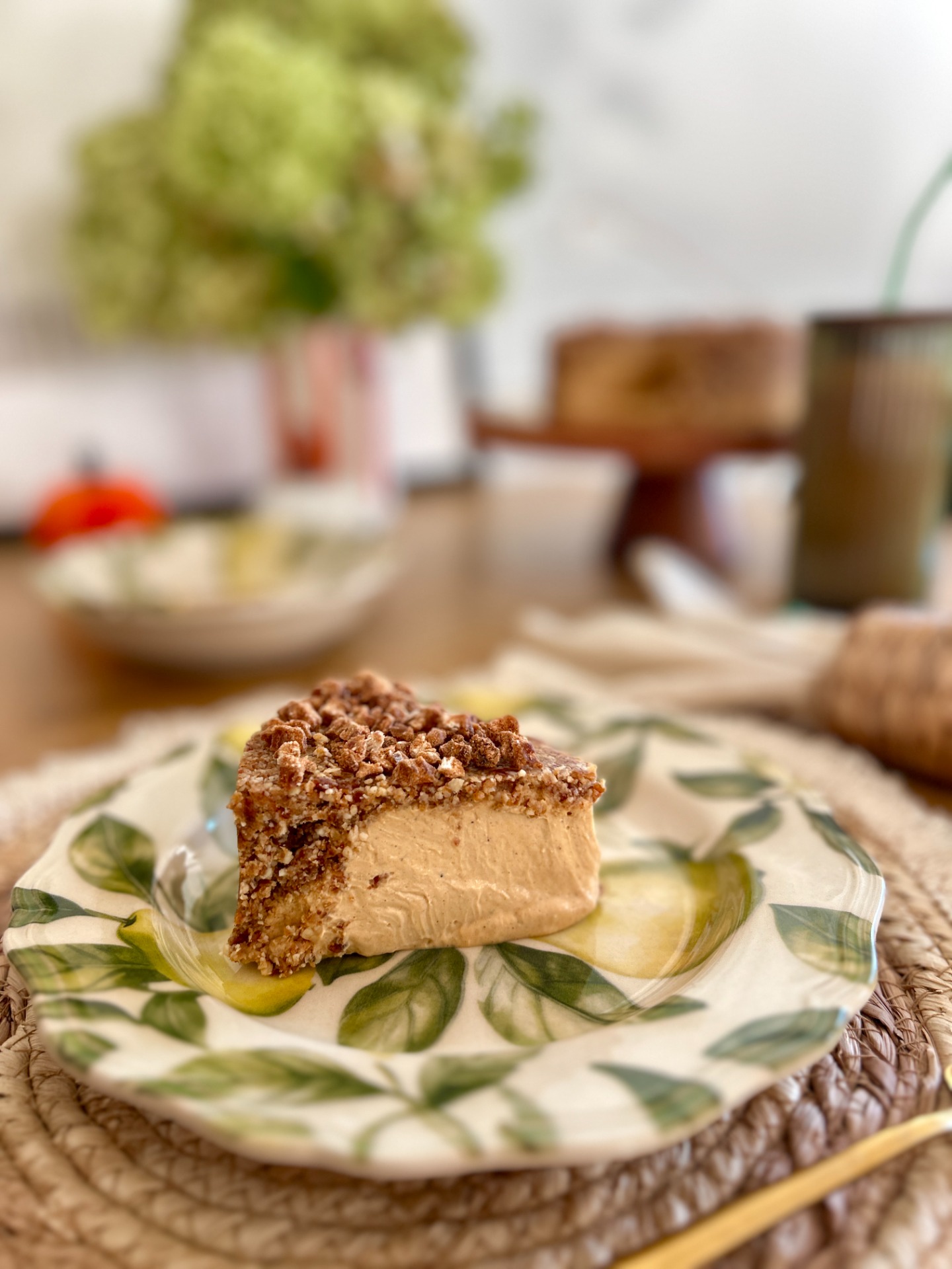 Egy szelet vegán Pumpkin Spice sajttorta vastag, narancssárga sütőtökös krémréteggel és rusztikus, mandulás-datolyás tetővel.
